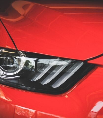 Detailed view of a red Ford Mustang's headlight showcasing sleek automotive design.